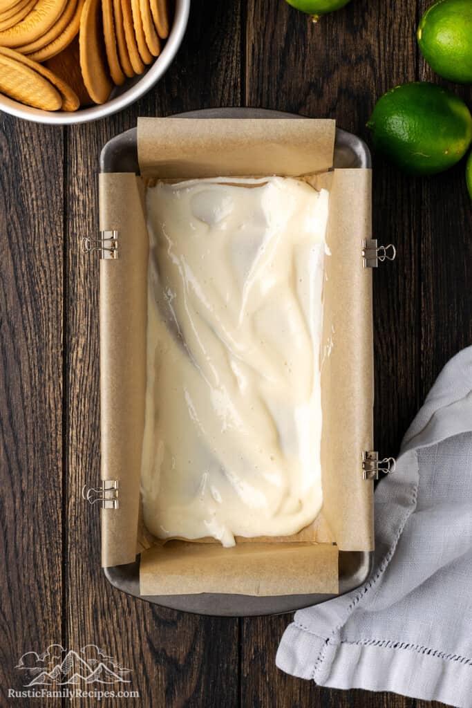 A layer of sweetened condensed milk in the bottom of a loaf pan lined with parchment paper.