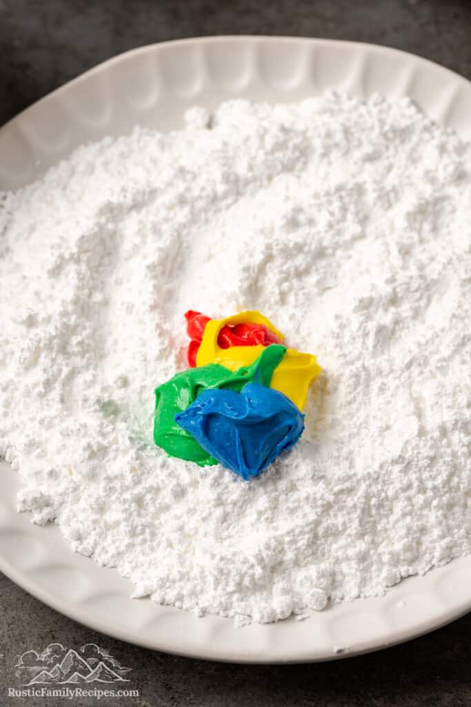 Colorful cookie dough being rolled in confectioners sugar