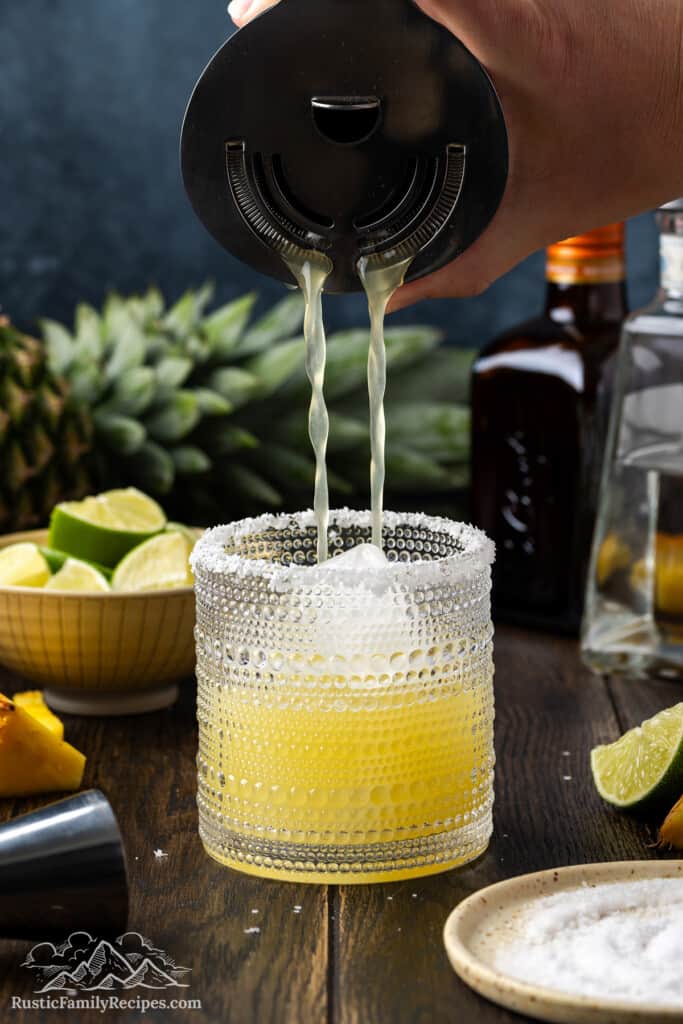 Straining pineapple margarita into a margarita glass with a salt rim
