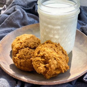 A glass of milk next to three pumpkin cookies
