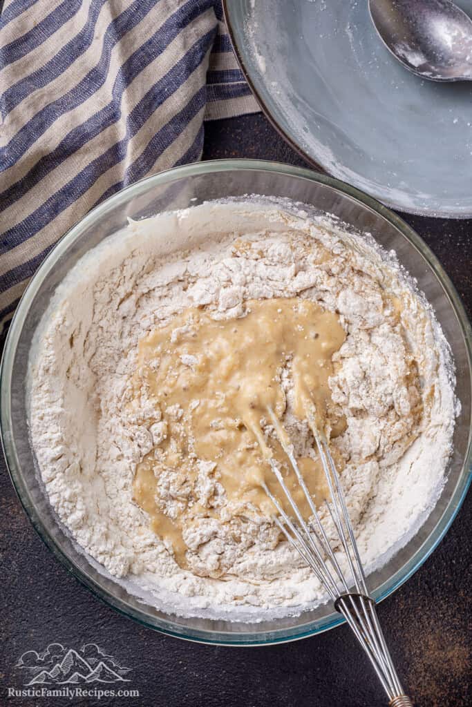 Dry ingredients whisked into wet muffin batter in a large glass bowl.