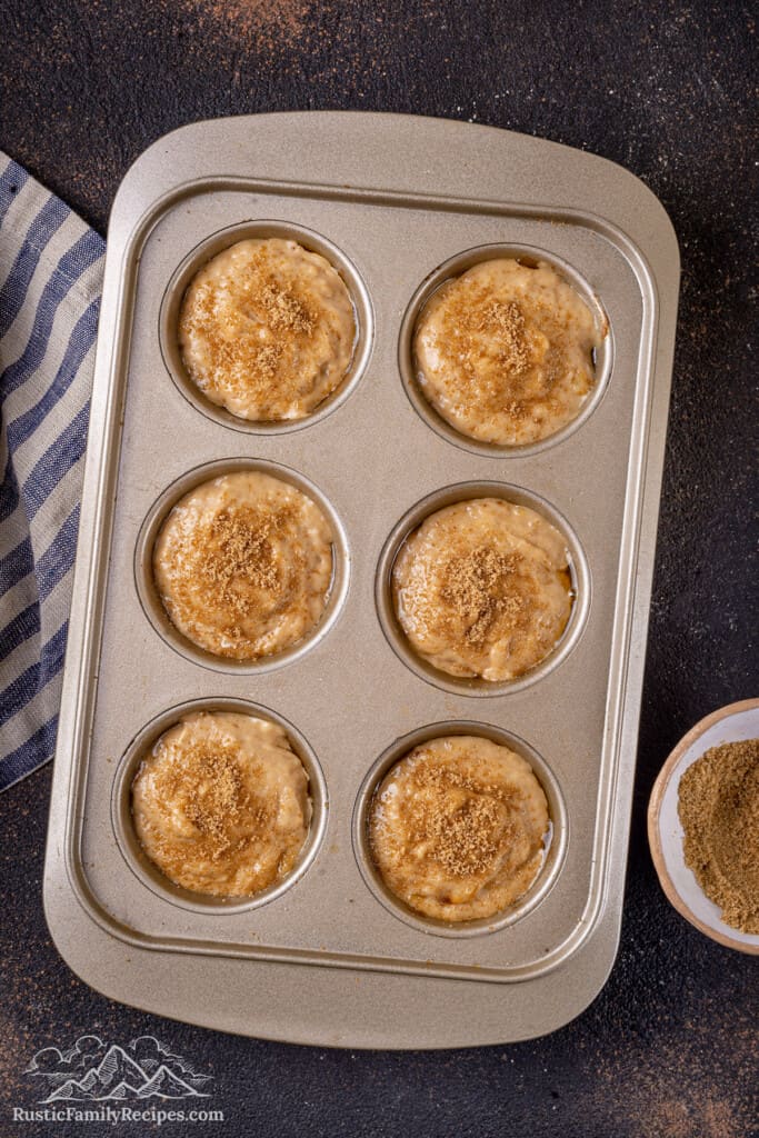 Overhead view of unbaked banana bread muffin batter in a muffin tin topped with raw sugar.
