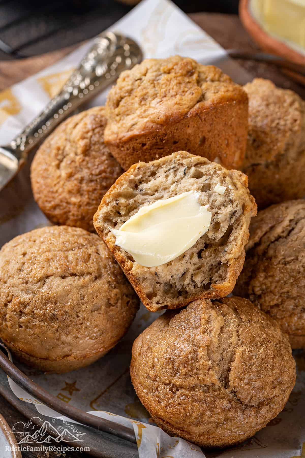 Close up overhead view of a bowl of banana bread muffins with one half of a muffin spread with butter.