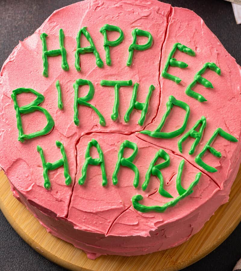 Overhead close up view of a Harry Potter birthday cake frosted with pink frosting and "Happy Birthday Harry" written on top with green icing.