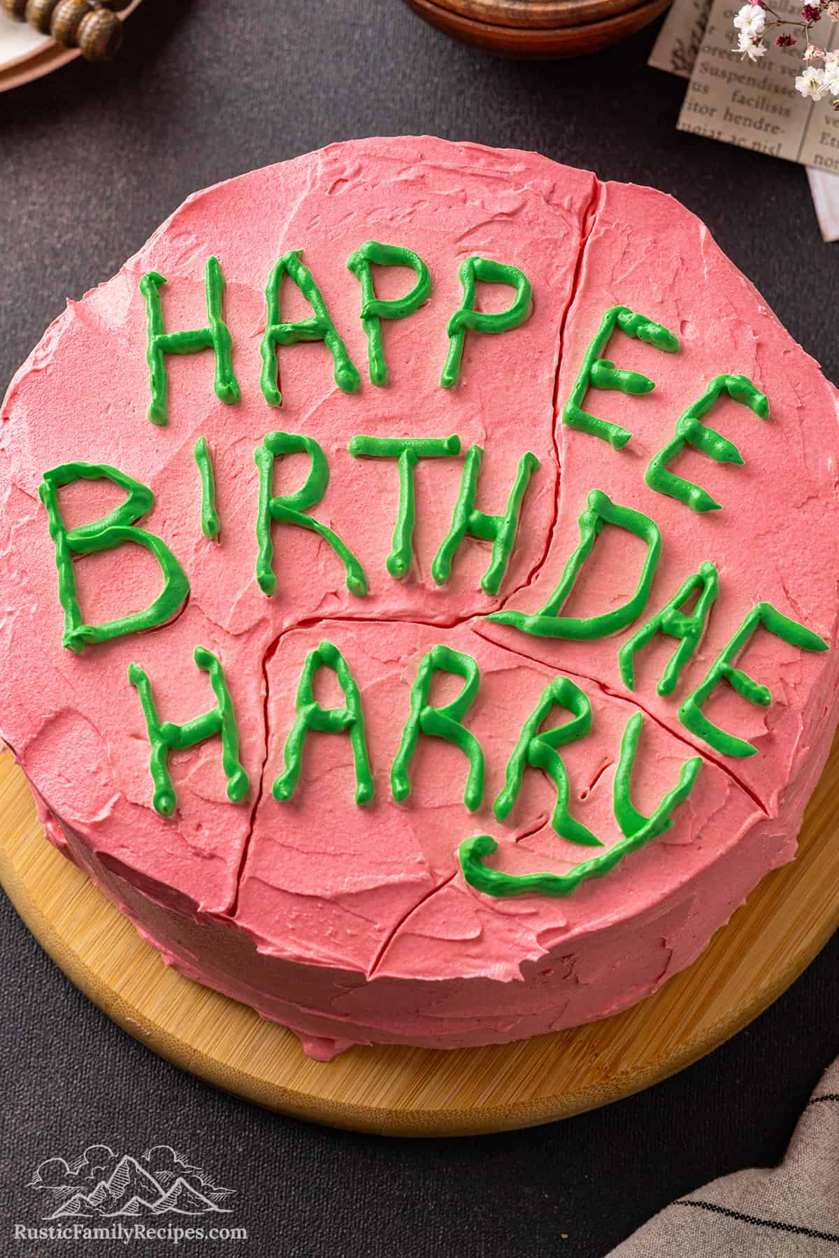 Overhead close up view of a Harry Potter birthday cake frosted with pink frosting and "Happy Birthday Harry" written on top with green icing.