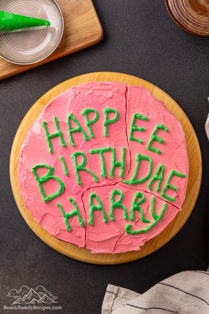 Overhead view of a Harry Potter birthday cake frosted with pink frosting and "Happy Birthday Harry" written on top with green icing.