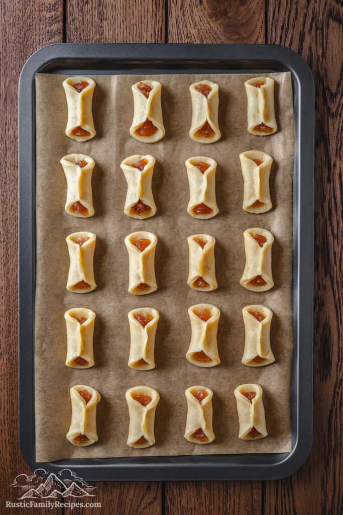 Overhead view of rows of unbaked jam-filled pizzicati cookies on a parchment-lined baking sheet.