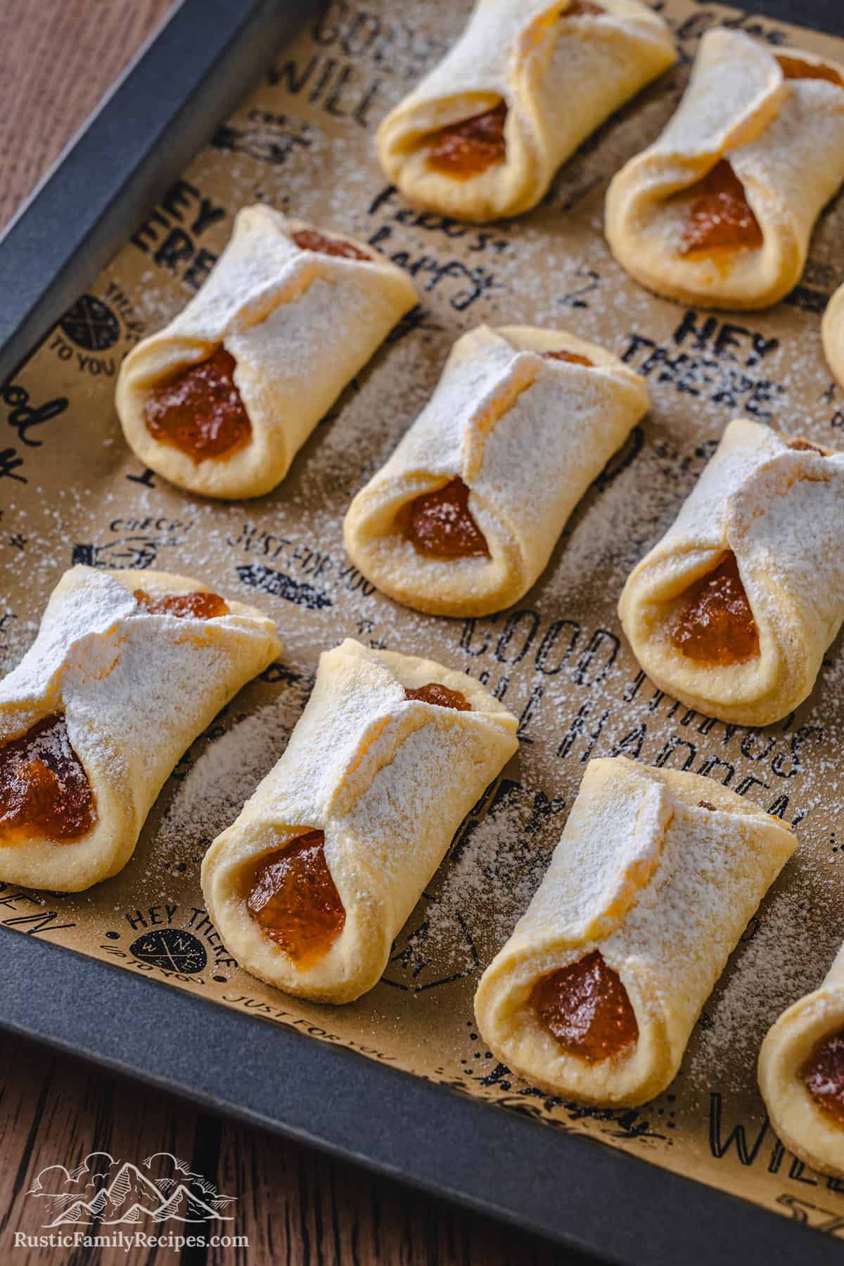 Rows of jam-filled pizzicati cookies dusted with powdered sugar on a parchment-lined baking sheet.