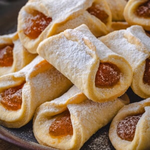 Close up of assorted pizzicati cookies filled with jam and dusted with powdered sugar on a dark plate.