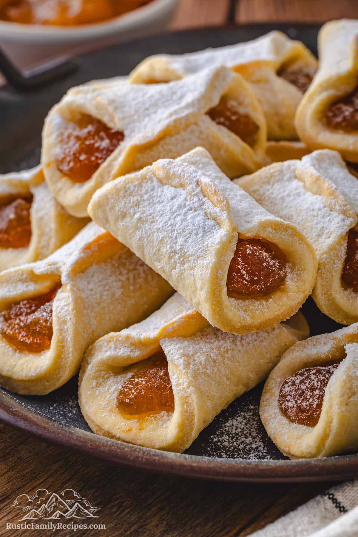 Close up of assorted pizzicati cookies filled with jam and dusted with powdered sugar on a dark plate.