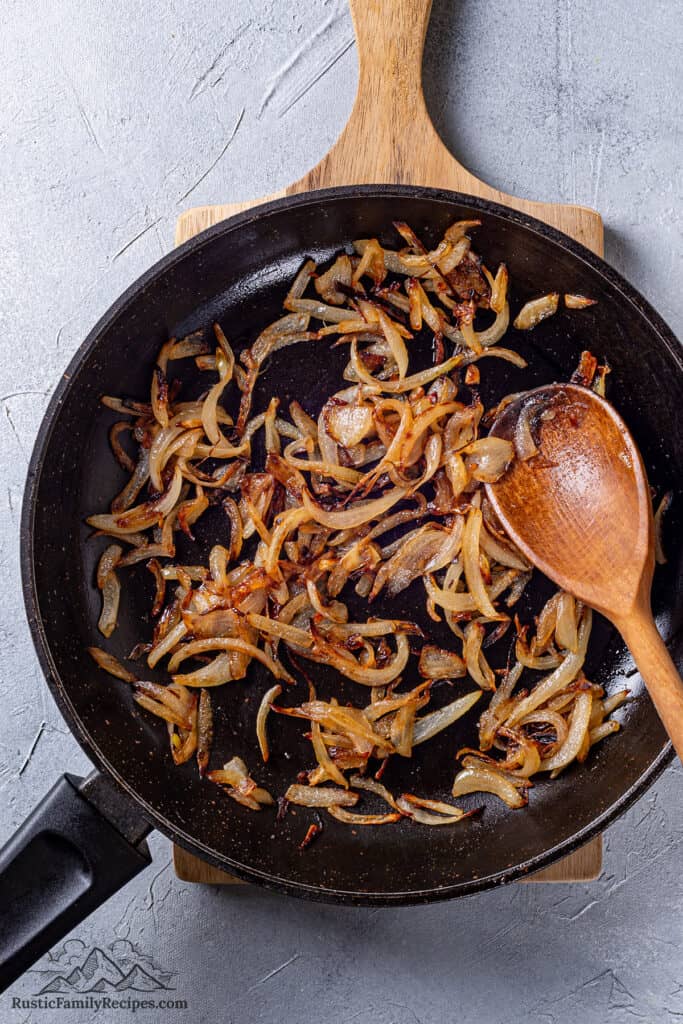 Caramelized onions in a skillet with a wood spoon