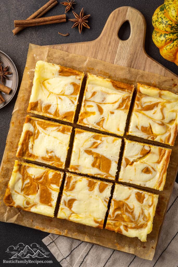 Overhead view of pumpkin cheesecake bars on a wooden cutting board.
