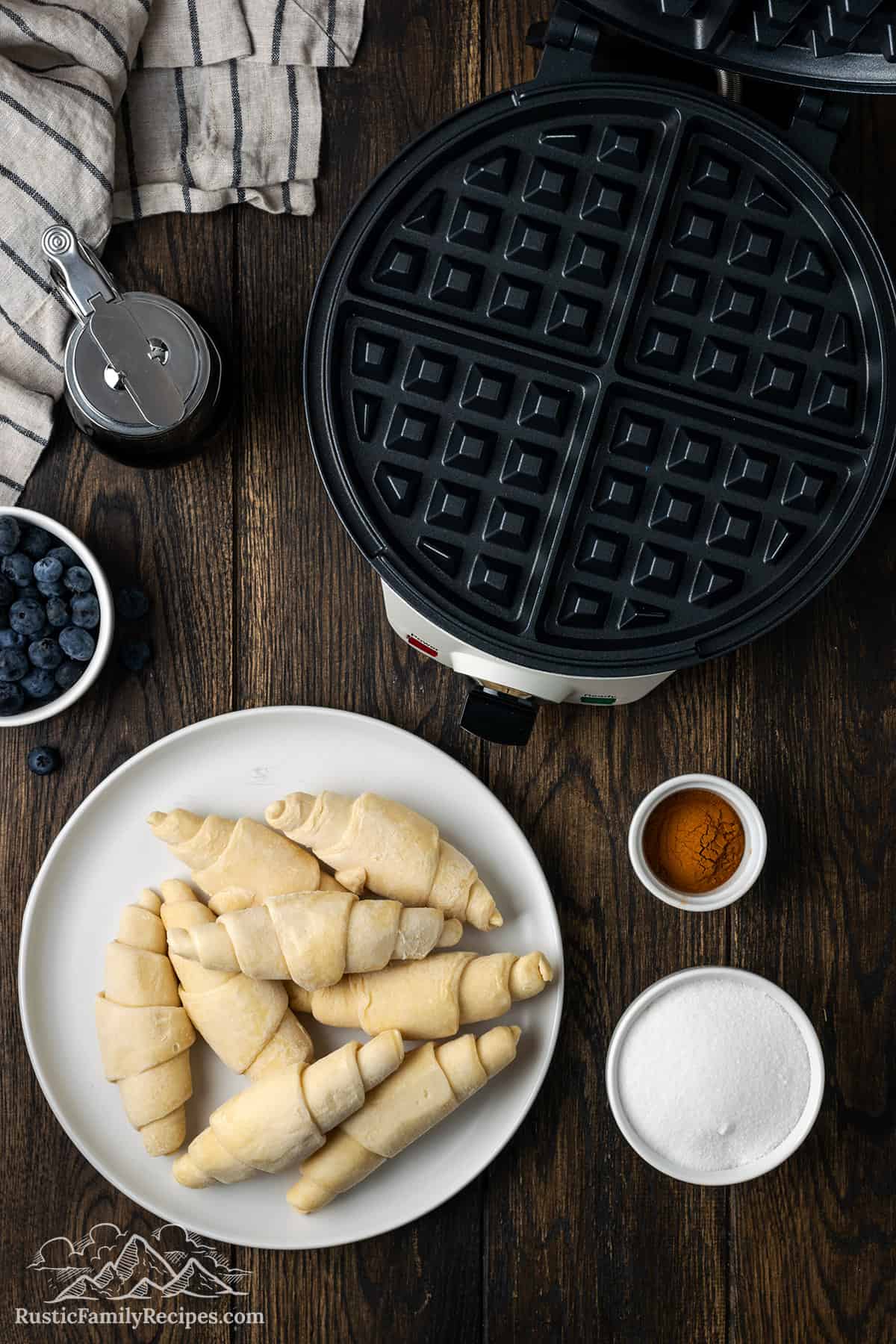 Top view of waffle maker, mini croissants, cinnamon and sugar