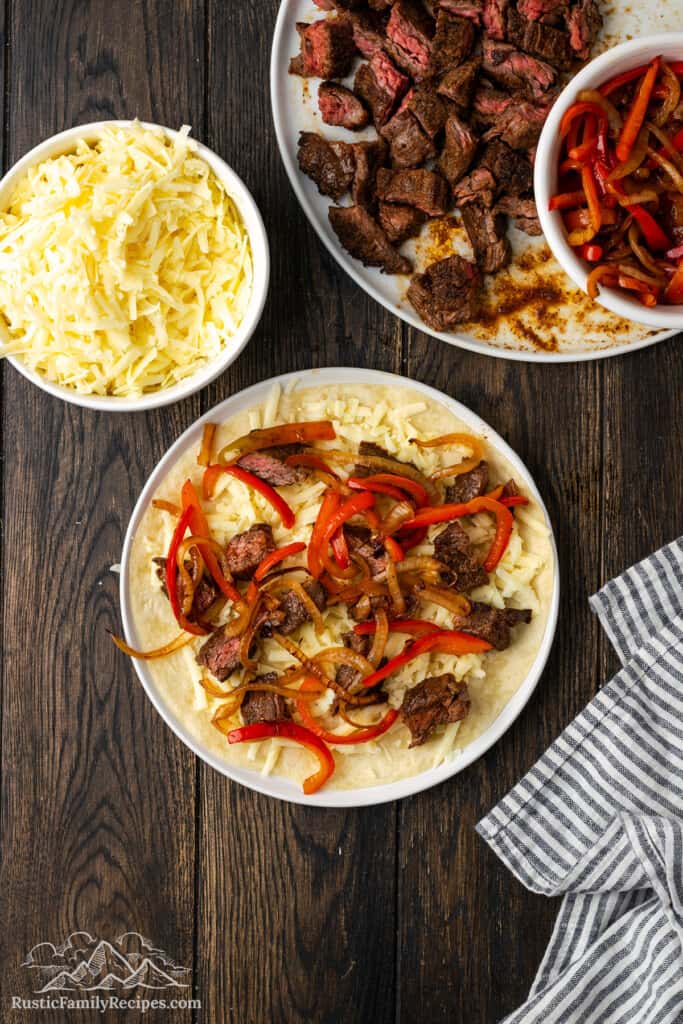 Adding steak, onions and peppers to a quesadilla.