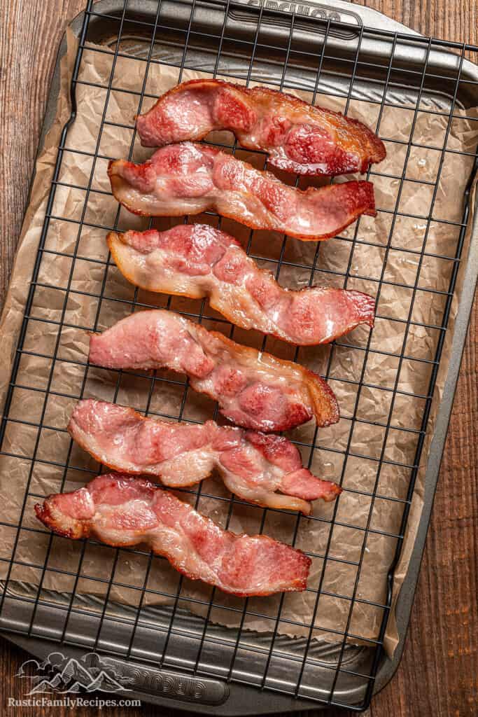 Cooked bacon strips on a rack over a baking sheet.