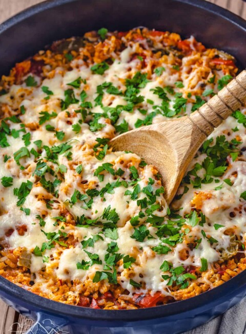 Close up of stuffed pepper casserole in a large Dutch oven with a wooden spoon for serving.