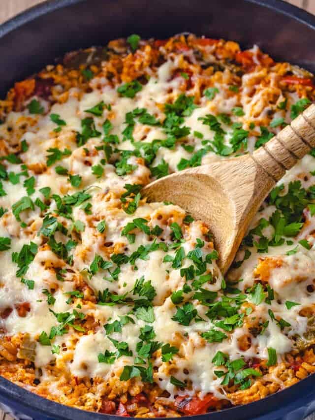 Close up of stuffed pepper casserole in a large Dutch oven with a wooden spoon for serving.