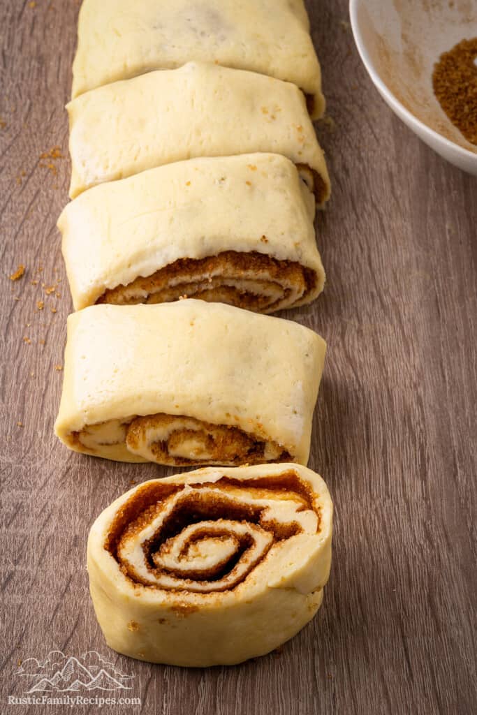 Rolled up dough being cut into cinnamon rolls.