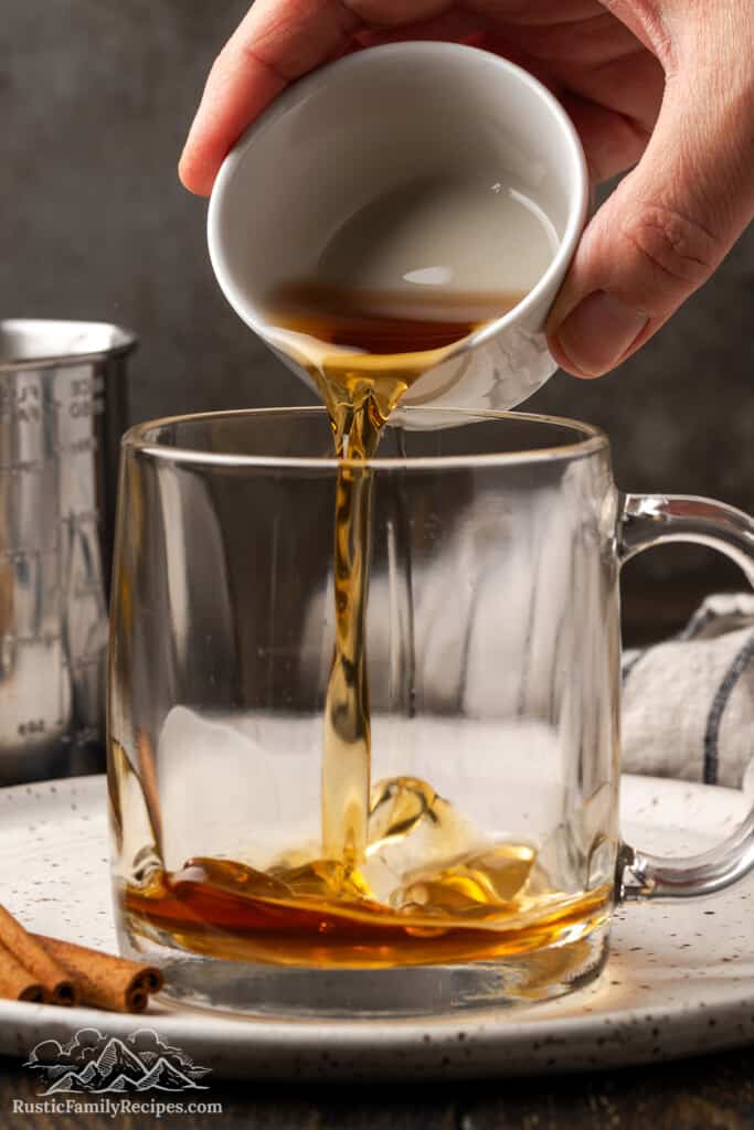 Pouring cinnamon simple syrup into a glass mug.