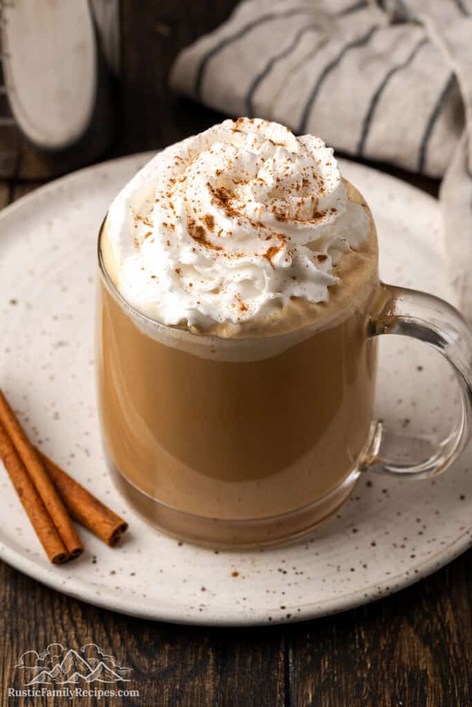 Coffee in a mug on a white plate, topped with whipped cream and cinnamon.