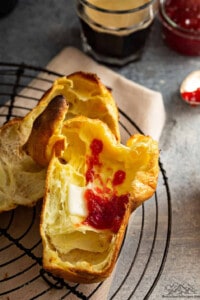 A sliced open popover with jam and butter inside.