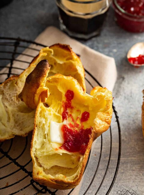 A sliced open popover with jam and butter inside.