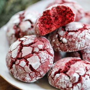 A white plate with a pile of red velvet crinkle cookies, a bite taken out of one.