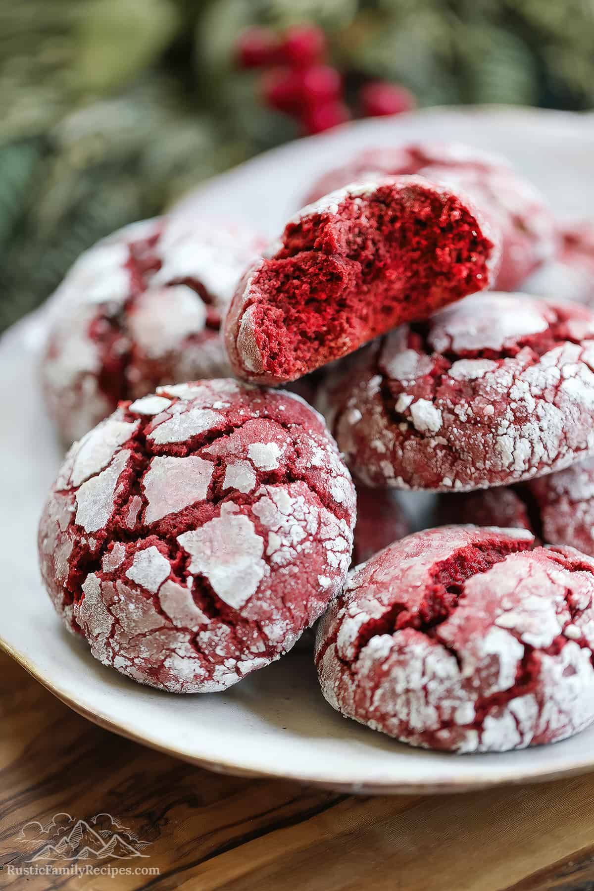 A white plate with a pile of red velvet crinkle cookies, a bite taken out of one.